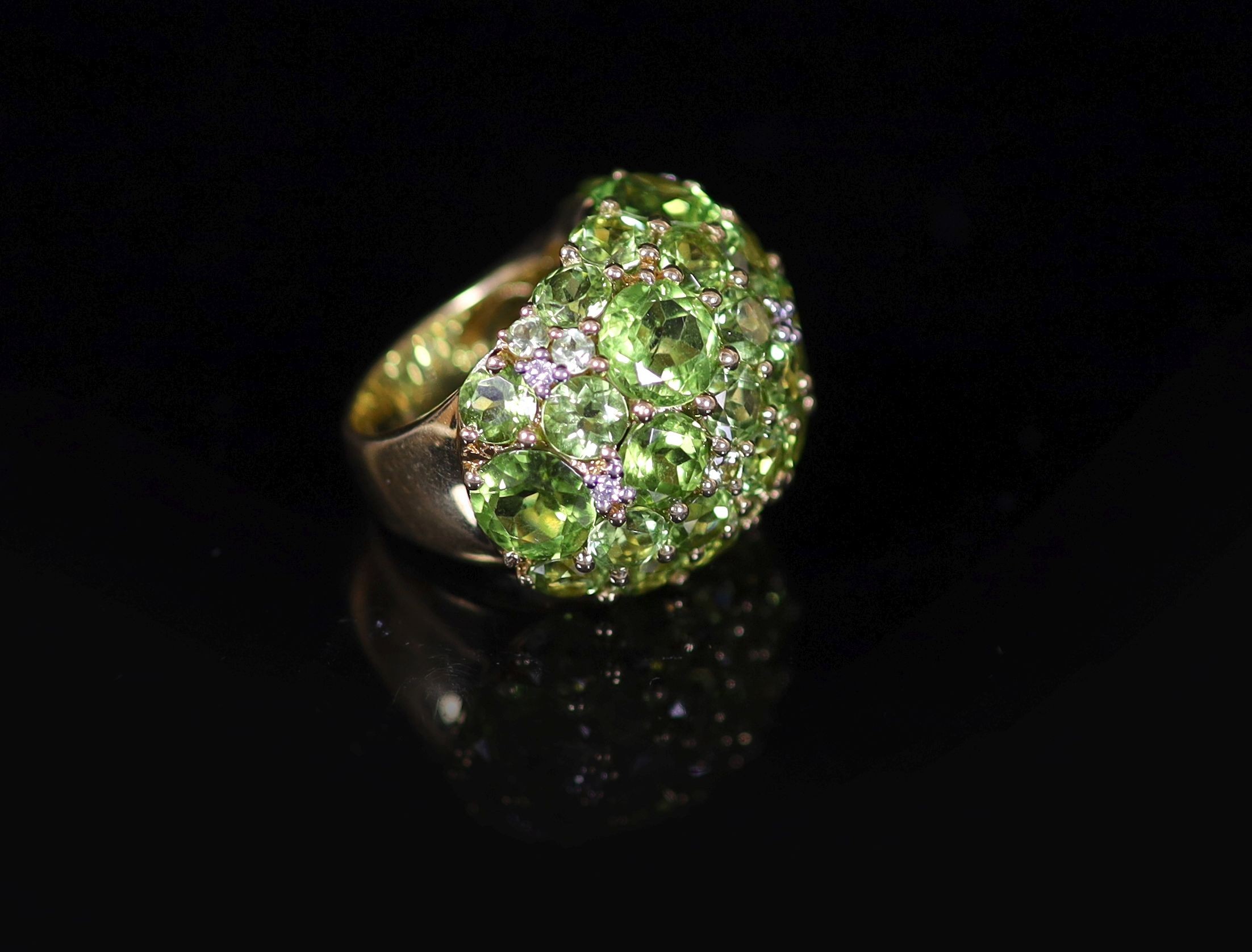 A Continental 18k gold and graduated round cut peridot encrusted dress ring, with diamond chip spacers